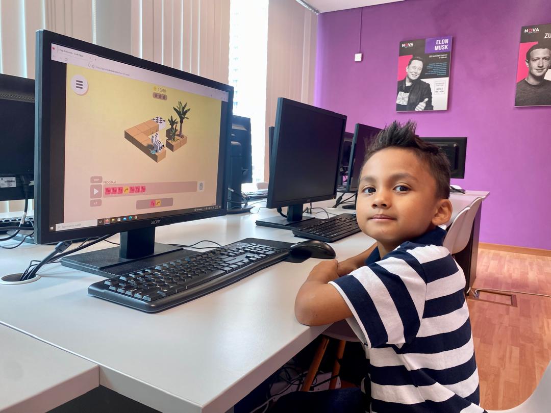 A young NOVA student smiling at the camera during a coding class